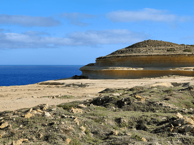 Klippefyldt kystplateau ved Dwejra på Gozo med lagdelte kalkstensklipper med udsigt over det dybtblå Middelhav under en delvist skyet himmel.