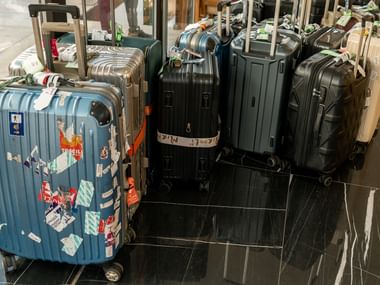 Samling af kufferter med hjul på marmorgulv, inklusive blå kuffert med rejsemærkater og sorte kufferter til Camino de Santiago rejse.