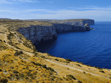 Stejle kalkstensklipper ved Dwejra på Gozo, Malta, med en vandesti langs den gyldne kystlinje med udsigt over det dybtblå Middelhav.