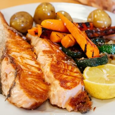 Grillet laksefilet med sitron, stekte grønnsaker inkludert gulrøtter, squash og poteter på hvit tallerken på dag 8 av Portugisisk Camino.
