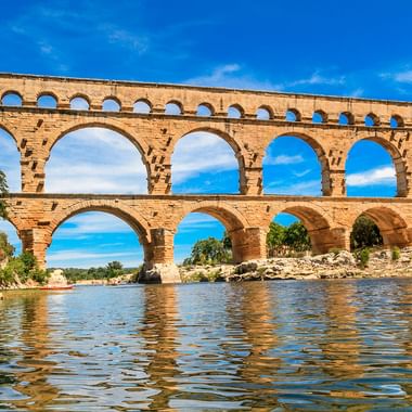 Antik romersk akvedukt Pont du Gard med tre nivåer av stenbågar över en flod i Provence, Frankrike, under blå himmel.