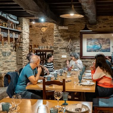 Gruppe af Camino de Santiago-pilgrimme spiser i en traditionel restaurant med stenvægge, synlige træbjælker og rustik indretning.