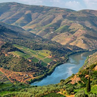 Naturskøn dal med en snoende flod gennem terrasserede skråninger i efterårsfarver. Landbrugsmarker og vingårde dækker skråningerne.