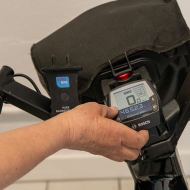 Närbild av en hand som använder en Bosch elcykel-display som visar hastighet och batterinivå, svart styre och kontrollenhet synlig.