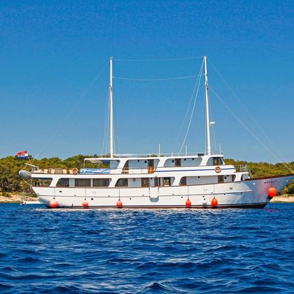 Hvid motoryacht MS Azimut med to master for anker i blåt vand nær den skovklædte kroatiske kyst under klar blå himmel.