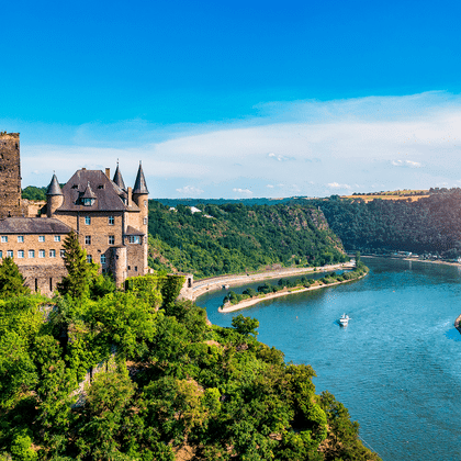Middelalderligt slot på en skovklædt bakke med udsigt over Rhinen nær Koblenz. Floden slynger sig gennem grønne bakker.