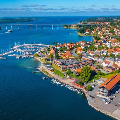Flygbild över Svendborg, Danmark som visar småbåtshamnen, färgglada hus, strandbyggnader och en bro över det blå vattnet.