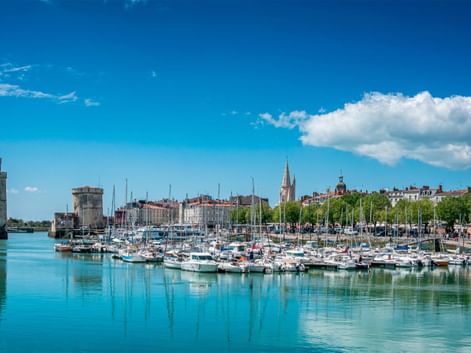 Marina i La Rochelle med talrige hvide sejlbåde fortøjet i roligt turkist vand. Middelalderlige stentårne vogter havneindgangen.