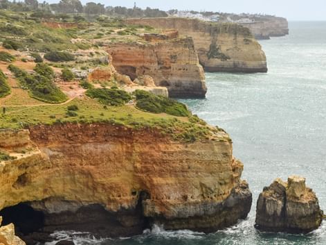 Gyldne kalkstensklipper langs Algarvekysten mellem Lagos og Tavira med grøn vegetation på toppen og turkisblåt havvand nedenfor.