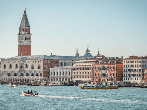 Venedigs vandkant med Markus Kampanile klokketårn, historiske bygninger og både på vandet. Klar himmel over den venetianske lagune.