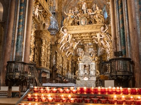 Interiør af Santiago de Compostela katedral med udsmykket barok alter med gyldne dekorationer og rækker af tændte bønelys.
