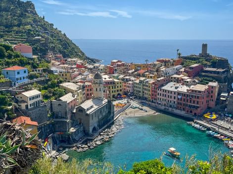 Aerial view of Vernazza, a colorful coastal village in Cinque Terre with a small harbor, historic tower, and buildings nestled between hillside and sea.