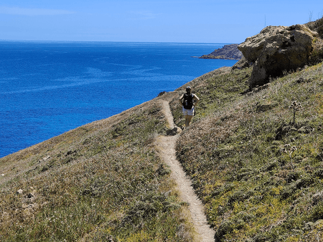 Vandrer på smal sti langs græsklædt kystskråning med udsigt over blåt Middelhav nær Ramla Beach, Gozo, Malta.