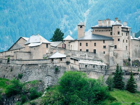 Château Queyras, en middelalderborg med stenmure og tårne, på en bakke i Ville-Vieille med skovklædte bjerge bagved.