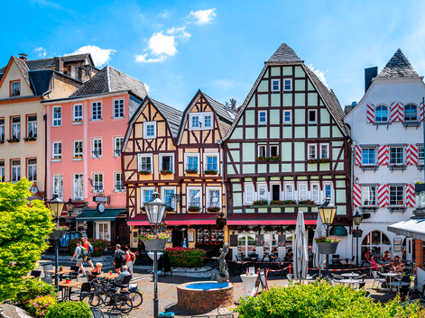 Farverige bindingsværkshuse og traditionelle bygninger omkring en offentlig plads i Linz med springvand, udendørs siddepladser og blå himmel.