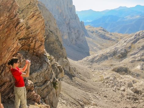 To vandrere på en klippefyldt bjergsti i Picos de Europa, Spanien. En person i rødt fotograferer de dramatiske kalkstenstinder.