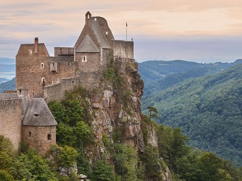 Middelalderlig stenburg på en klippefyldt klippe i Wachau-dalen, Østrig, med skovklædte bakker og Donau synlig i baggrunden.