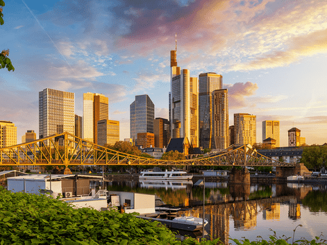 Frankfurt am Mains skyline med moderne skyskrabere reflekteret i Main. Gul jernbro krydser vandet, både fortøjet langs bredden.