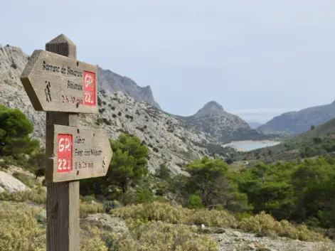 Tre-skilt for turstier med røde markeringer som viser retninger til forskjellige destinasjoner i steinete middelhavs-landskap.