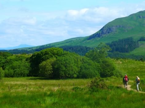 Fotturister på West Highland Way Skottland To fotturister går på en sti gjennom de grønne skotske høylandet med bølgende åser og fjell i bakgrunnen under en skyet himmel.