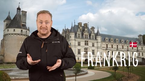 Mand i sort jakke gestikulerer foran fransk slot med teksten 'FRANKRIG' og dansk flag på YouTube-cover til Frankrig-rejseindhold.
