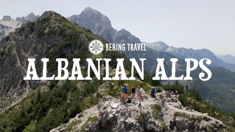 Gruppe vandrere på en smal fjelltopp i de albanske Alpene, med dramatiske fjelltopper og grønne daler i bakgrunnen.