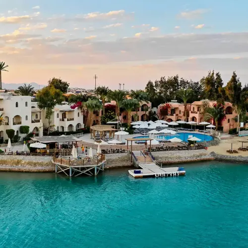 Luftfoto af Sultan Bey Hotel i El Gouna med hvide og terracottafarvede bygninger, pool og tyrkisblå lagune ved solnedgang.