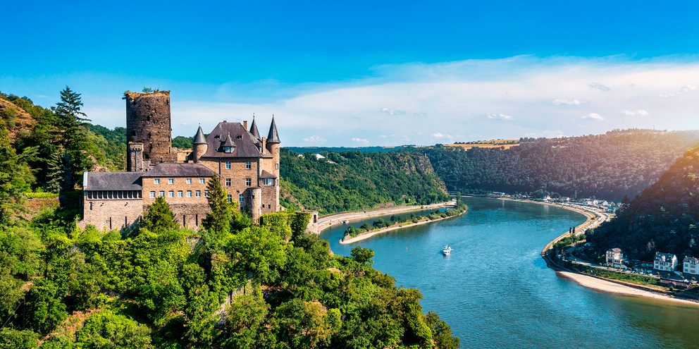 Middelalderligt slot på en skovklædt bakke med udsigt over Rhinen nær Koblenz. Floden slynger sig gennem grønne bakker.