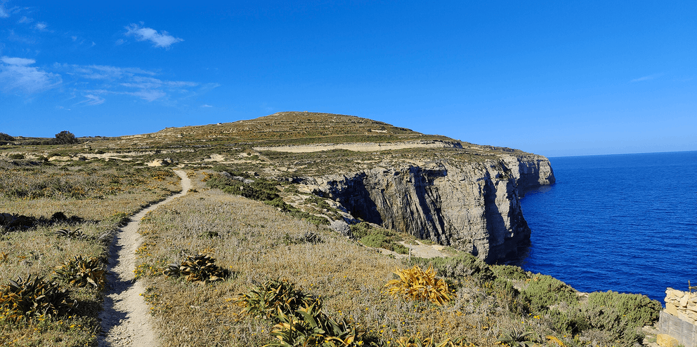 Vandrerute langs dramatiske kalkstensklipper nær Dwejra på Gozo, Malta. Stien slynger sig gennem sparsom vegetation med dybt blåt Middelhav.